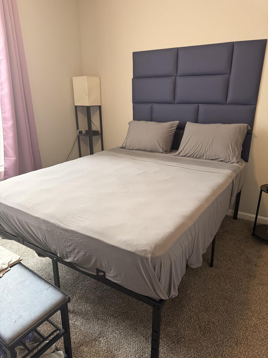 Gray sheets and two matching pillows on a bed with a tall dark blue padded headboard.