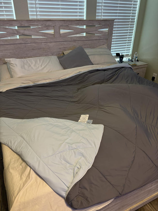 Gray comforter spread over a bed and folded back to reveal a pale blue reverse beneath a wooden headboard.
