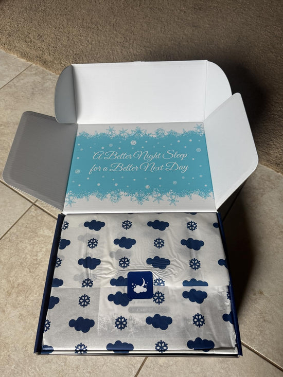Open Sleephoria box on carpet, with cloud and snowflake printed wrapping and a turquoise message inside the lid.