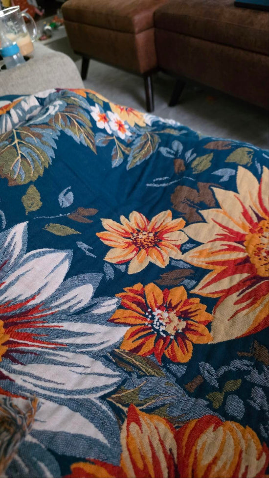 Close-up of a blue woven throw with large white, yellow and orange flowers draped in a living room.