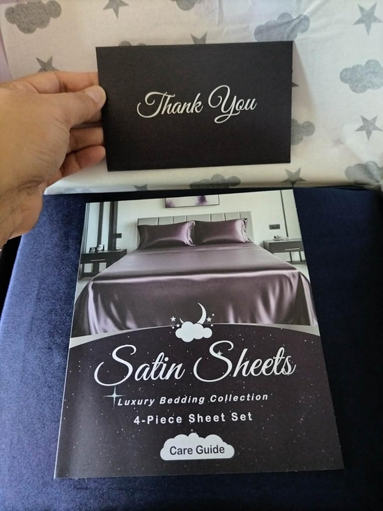 Hand holding a black Thank You card over an open package and a Satin Sheets care guide.