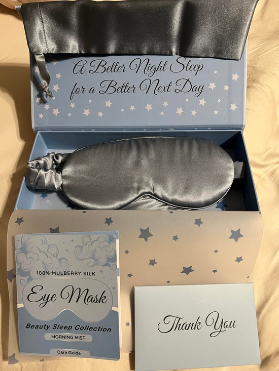 Silver gray sleep mask in an open star patterned box beside its care guide and Thank You card.