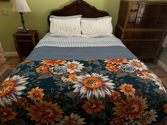 Blue throw with large yellow, orange and white flowers spread across the foot of a bed.