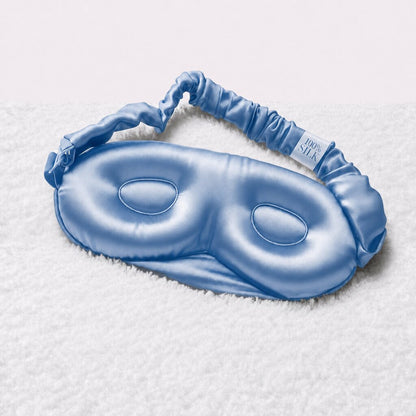 Inside of a blue contoured sleep mask resting on a white towel, showing recessed eye cups and a gathered adjustable strap.
