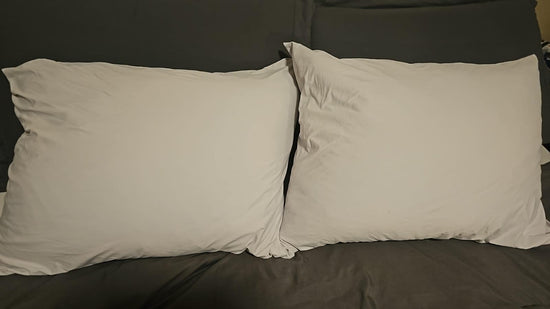 Two white pillows placed side by side against dark bedding.