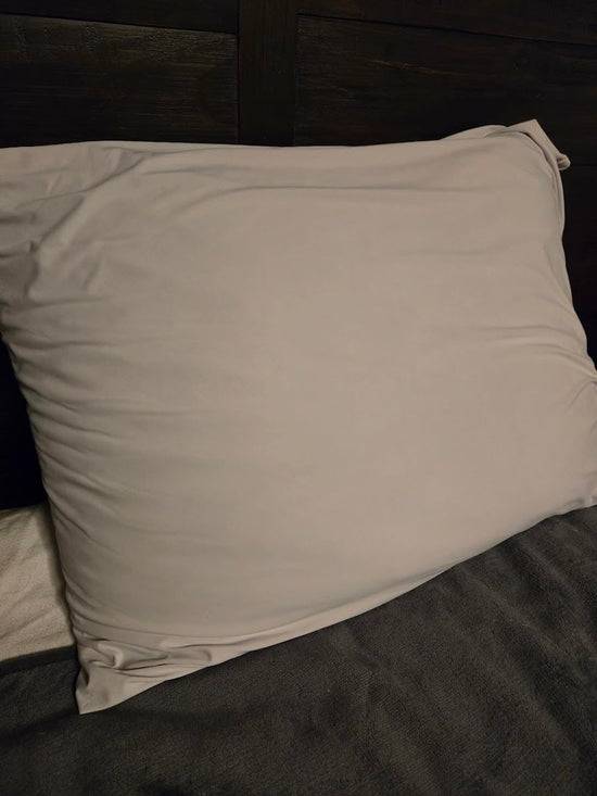 Close view of a pale gray pillowcase on a pillow against a dark wooden headboard.