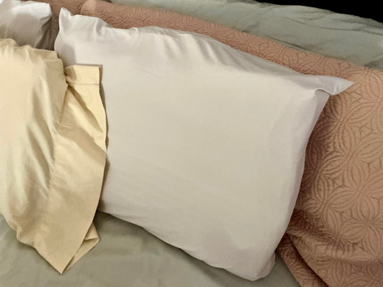 White pillow in front of a pink patterned pillow, with cream fabric draped over its side.