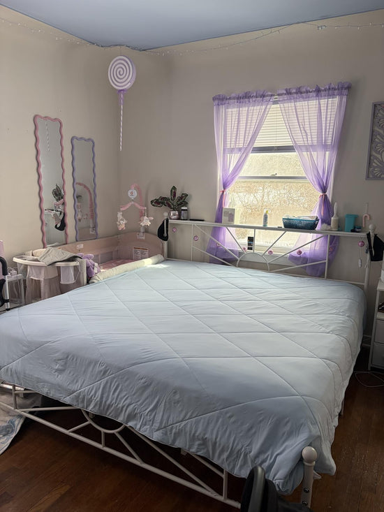Light blue diamond quilted comforter on a metal bed frame in a bedroom with lavender curtains.