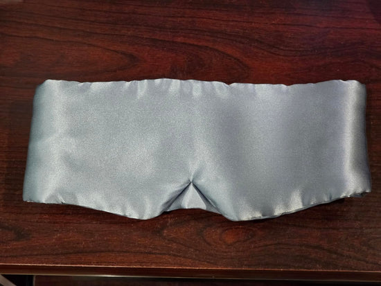 Pale blue wide sleep mask laid flat on a dark wooden surface, showing a central nose seam.