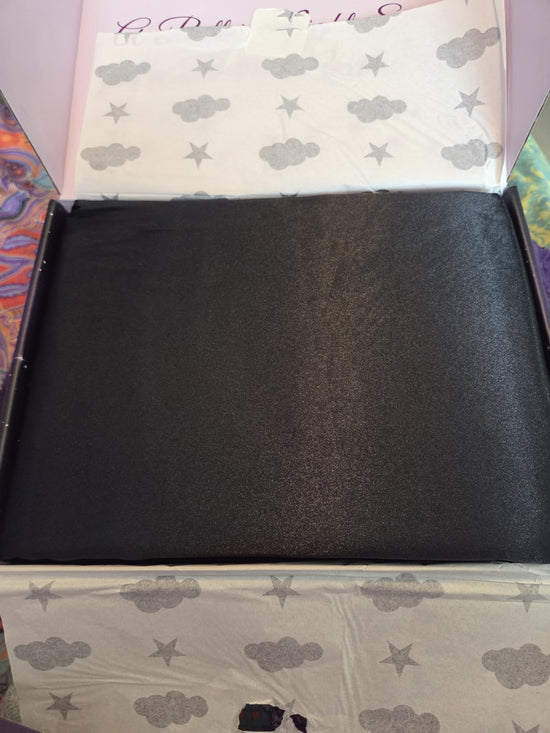 Folded black satin fabric inside an open box lined with a cloud and star pattern.