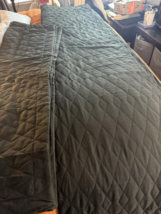 Dark green diamond quilt spread across a bed with a matching sham laid on top.