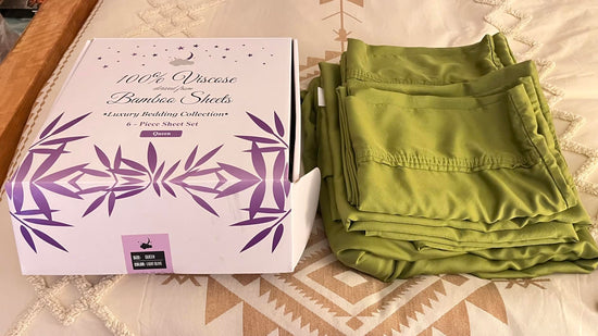 Folded olive green sheets beside an open bamboo sheet package on patterned bedding.
