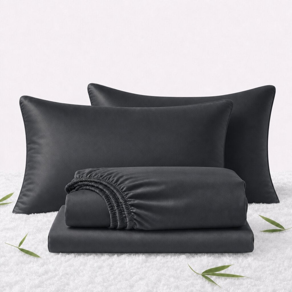 Folded black sheets in front of 2 matching pillows on a white textured surface with scattered bamboo leaves.