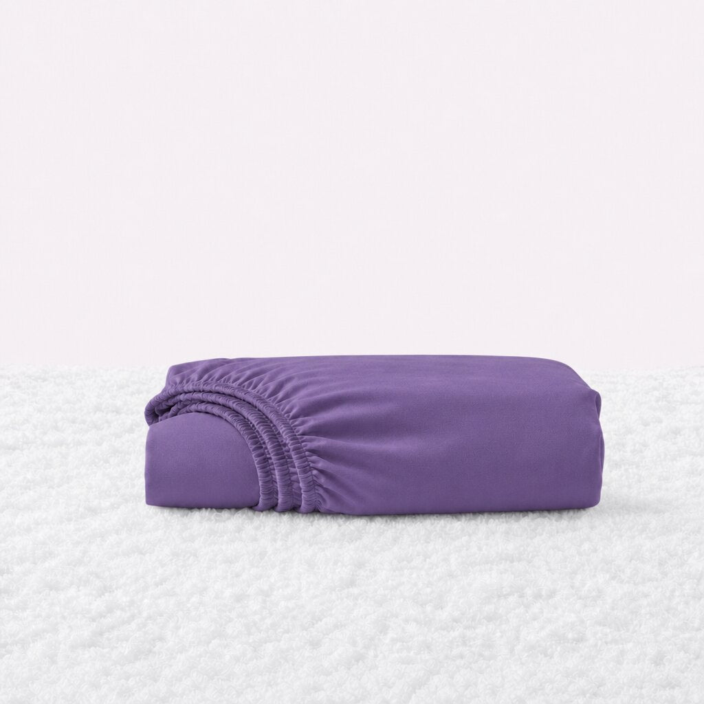 Folded purple fitted sheet with its gathered elastic edge visible on a white textured surface.