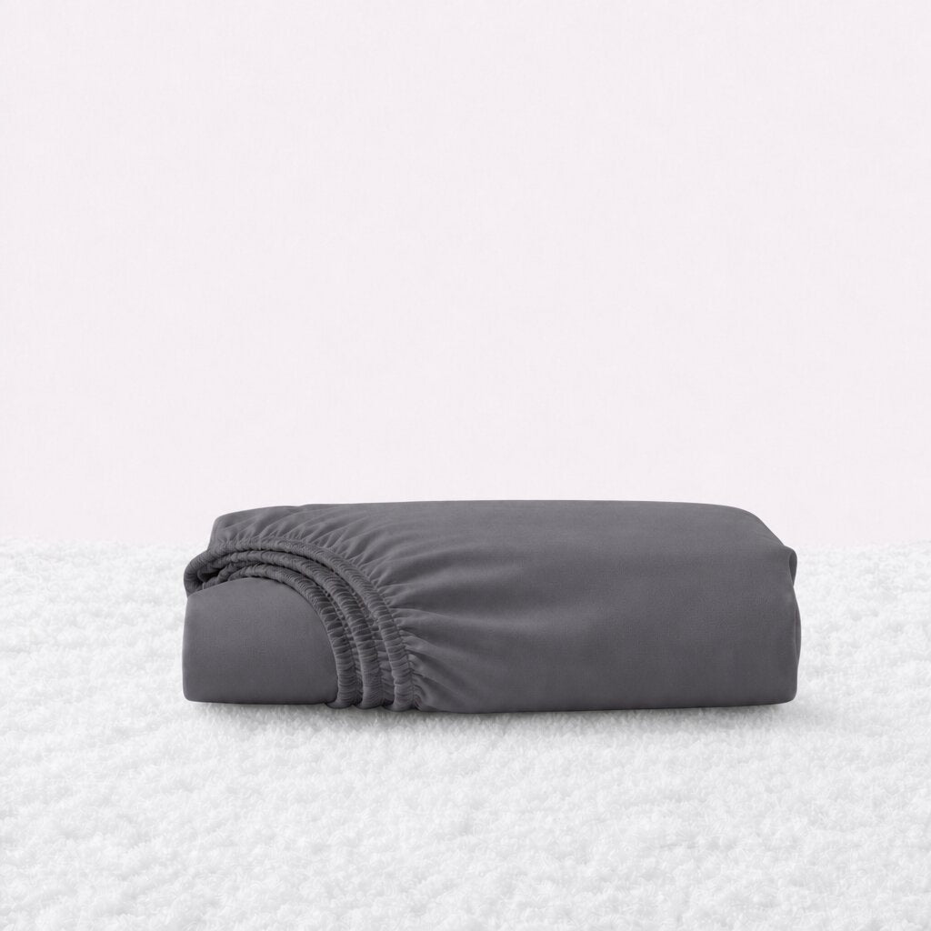 Folded charcoal gray fitted sheet with its gathered elastic edge visible on a white textured surface.