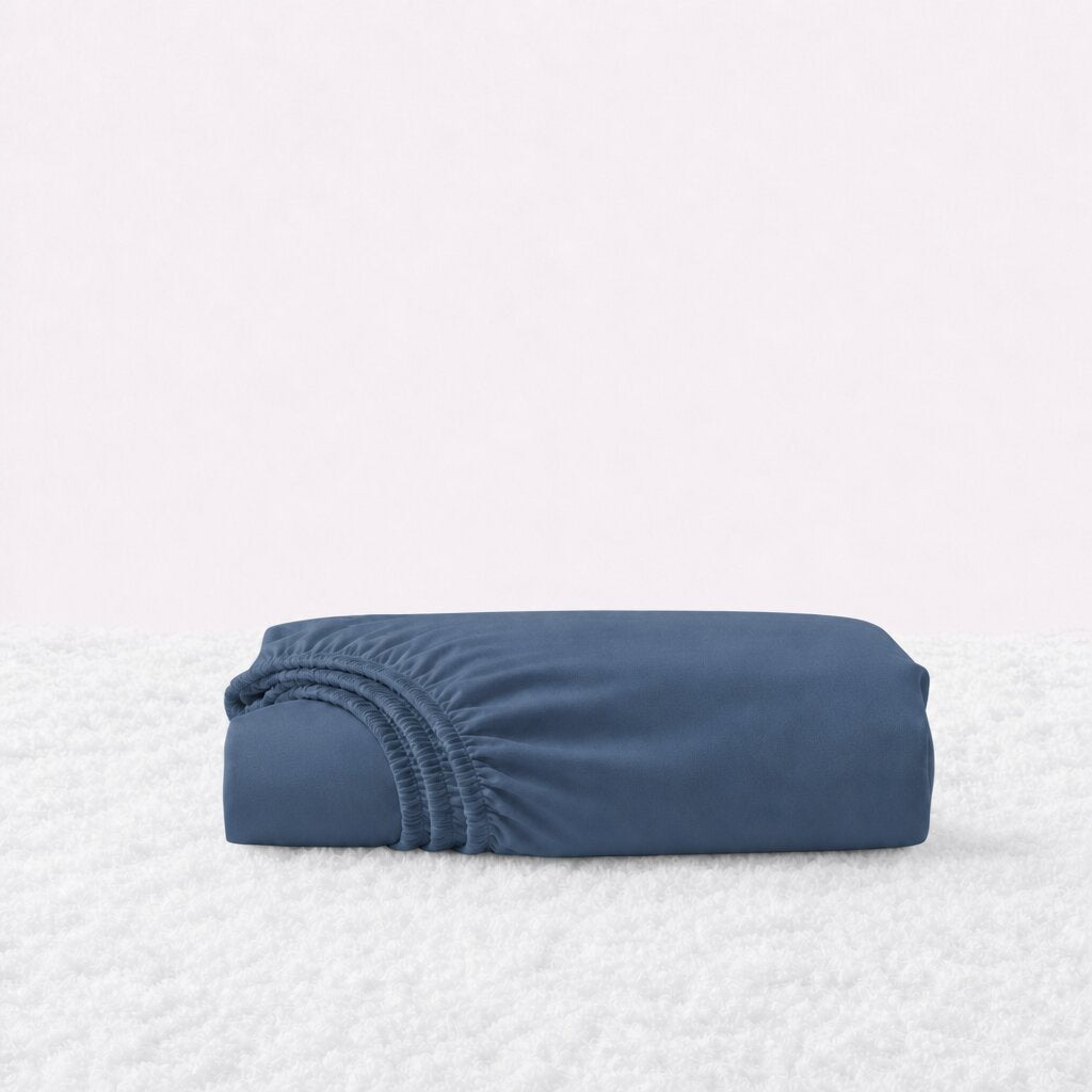 Folded navy blue fitted sheet with its gathered elastic edge visible on a white textured surface.