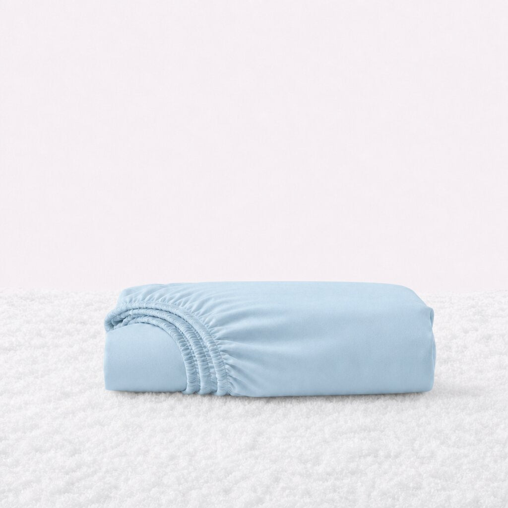 Folded light blue fitted sheet with its gathered elastic edge visible on a white textured surface.