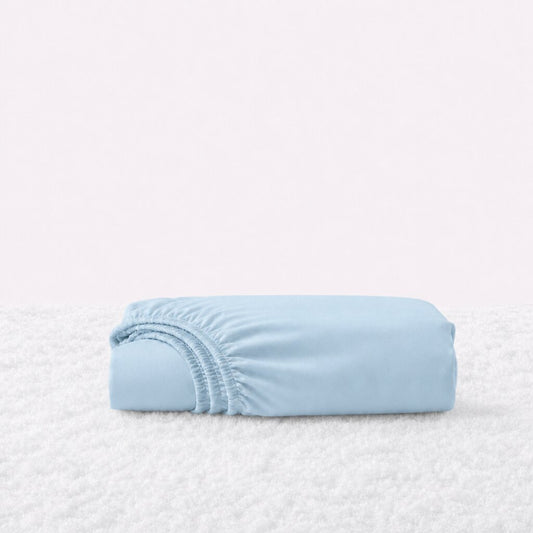 Folded light blue fitted sheet with its gathered elastic edge visible on a white textured surface.