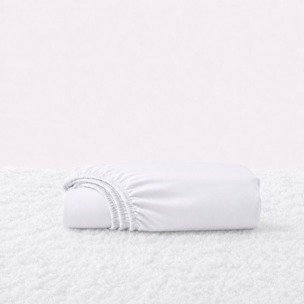 Folded white fitted sheet with its gathered elastic edge visible on a white textured surface.
