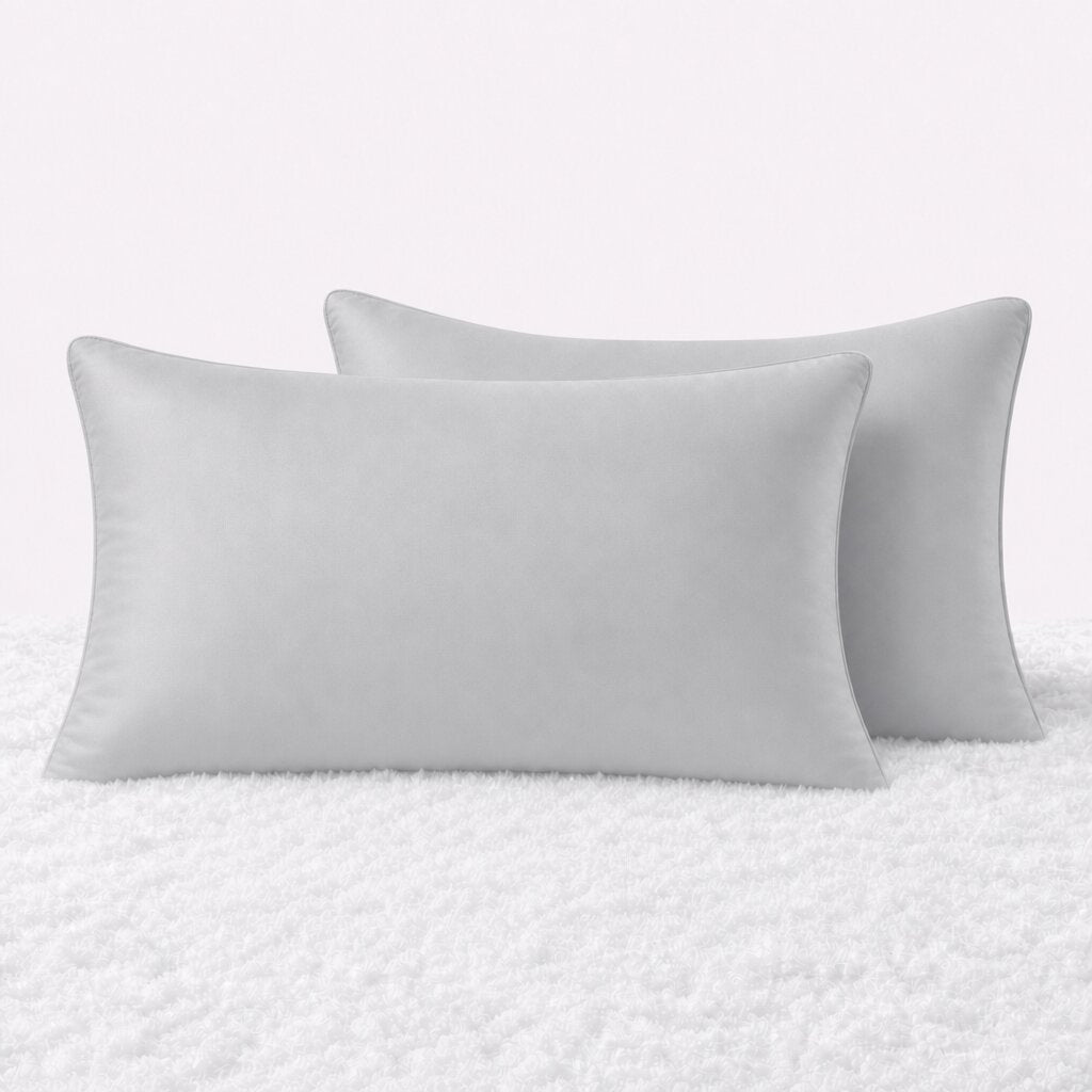 Two pillows in light gray pillowcases arranged upright on a white textured surface.