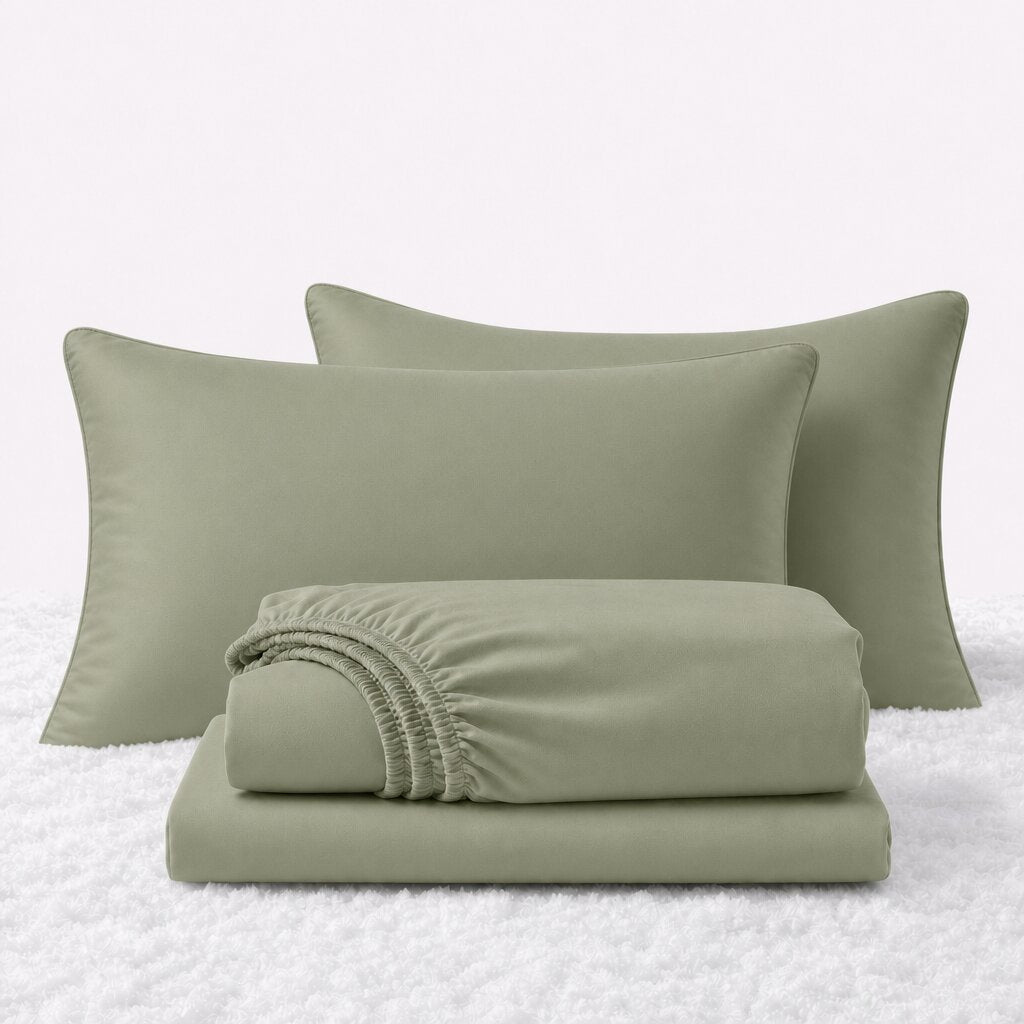 Sage green sheet set displayed with two pillows behind a folded fitted sheet and flat sheet on a white textured surface.