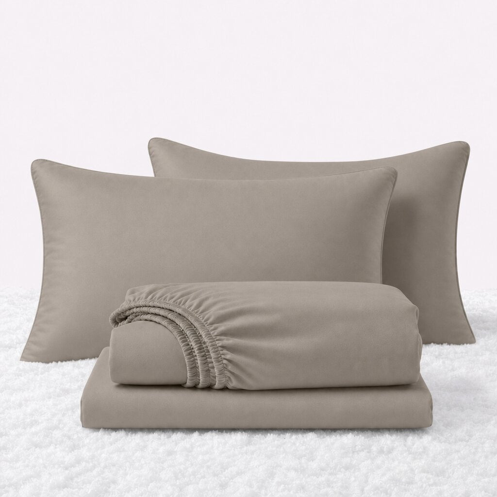 Beige sheet set displayed with two pillows behind a folded fitted sheet and flat sheet on a white textured surface.