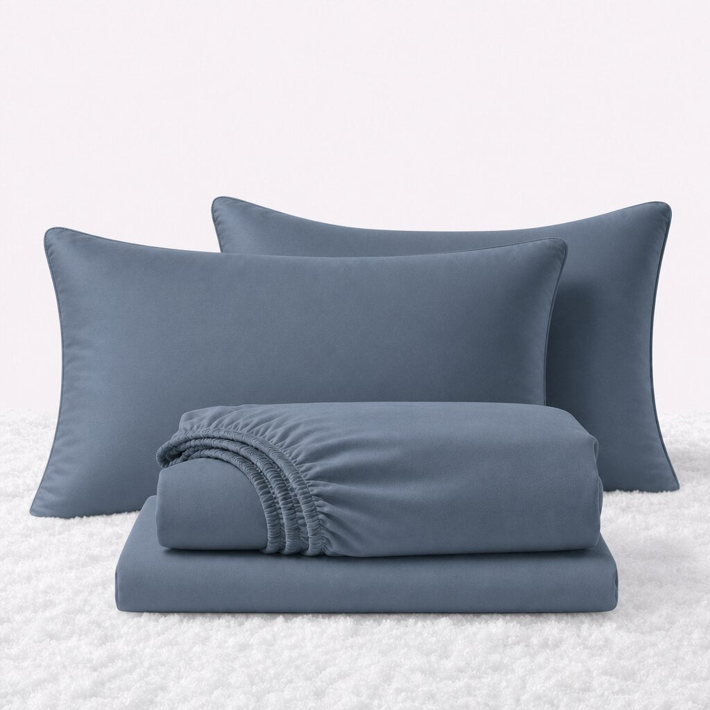 Navy blue sheet set displayed with two pillows behind a folded fitted sheet and flat sheet on a white textured surface.