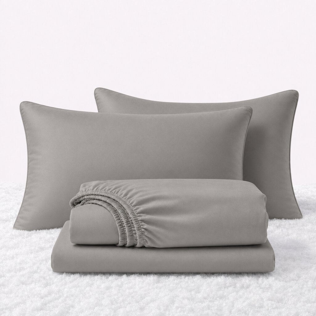Light gray sheet set displayed with two pillows behind a folded fitted sheet and flat sheet on a white textured surface.