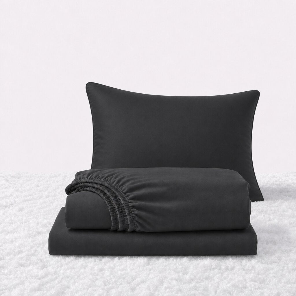 Black sheet set displayed with one pillow behind a folded fitted sheet and flat sheet on a white textured surface.