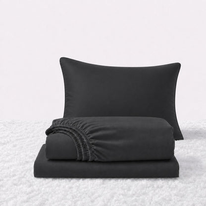 Black sheet set displayed with one pillow behind a folded fitted sheet and flat sheet on a white textured surface.