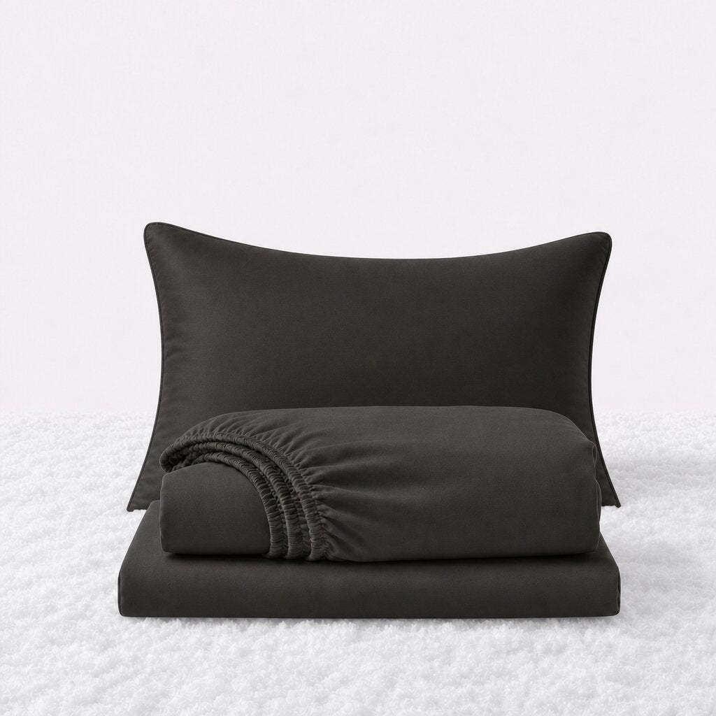 Charcoal gray sheet set displayed with one pillow behind a folded fitted sheet and flat sheet on a white textured surface.