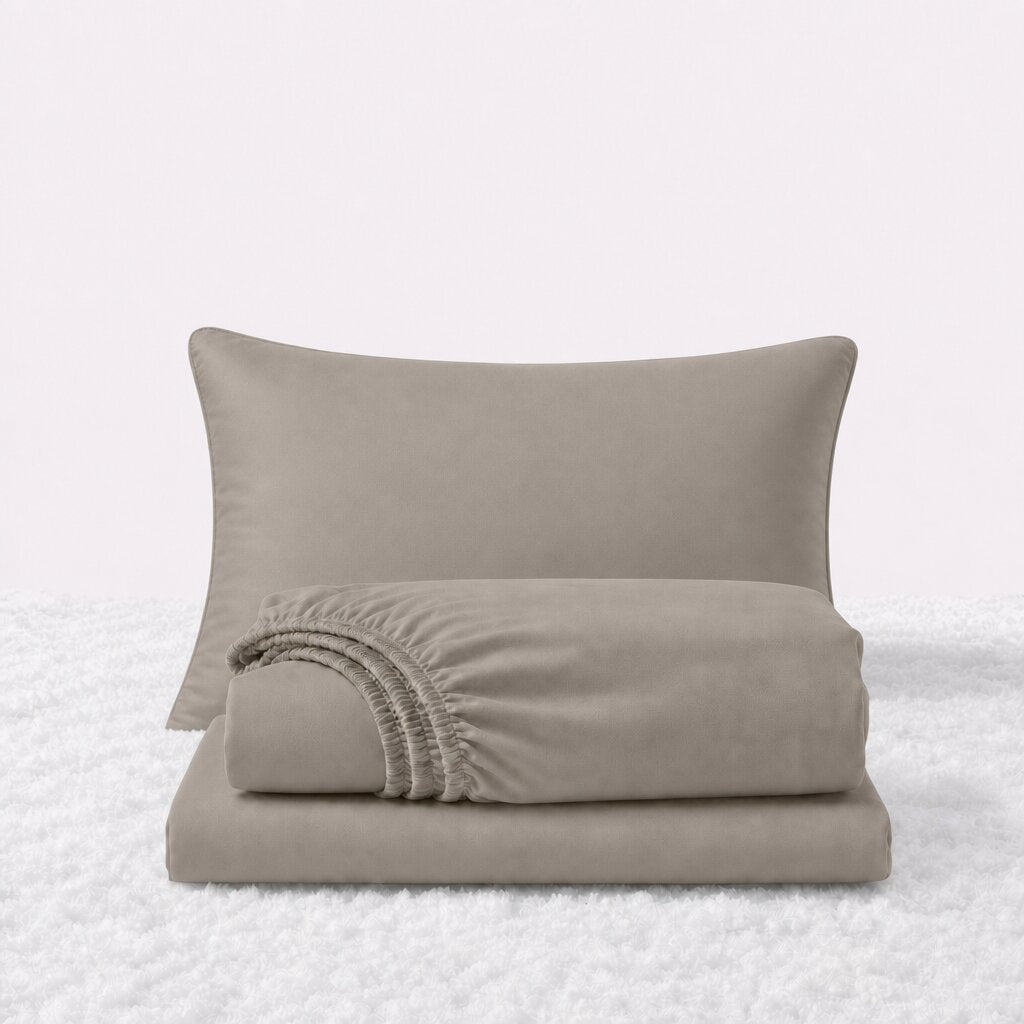 Beige sheet set displayed with one pillow behind a folded fitted sheet and flat sheet on a white textured surface.