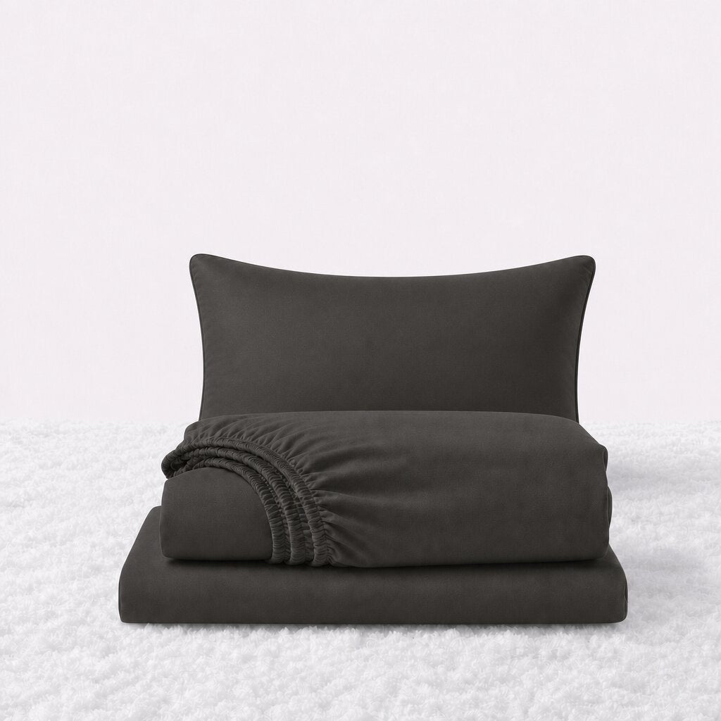 Dark gray sheet set displayed with one pillow behind a folded fitted sheet and flat sheet on a white textured surface.