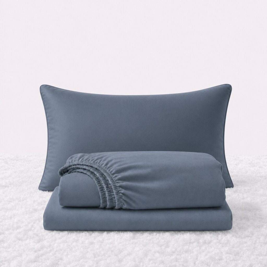 Navy blue sheet set displayed with one pillow behind a folded fitted sheet and flat sheet on a white textured surface.