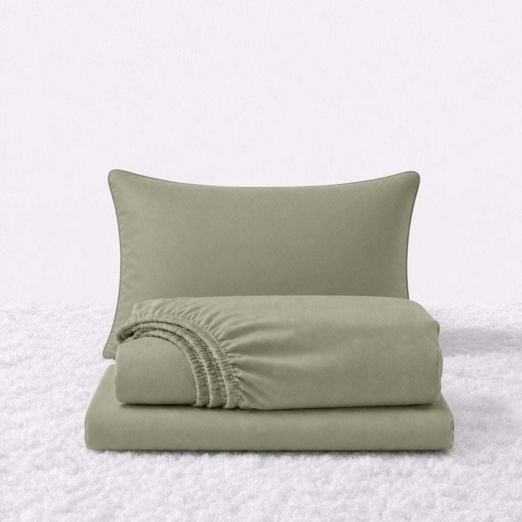 Sage green sheet set displayed with one pillow behind a folded fitted sheet and flat sheet on a white textured surface.
