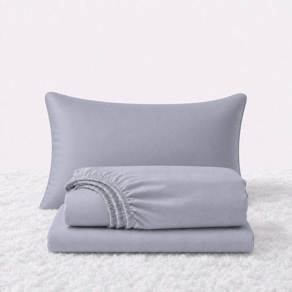 Pale blue gray sheet set displayed with one pillow behind a folded fitted sheet and flat sheet on a white textured surface.