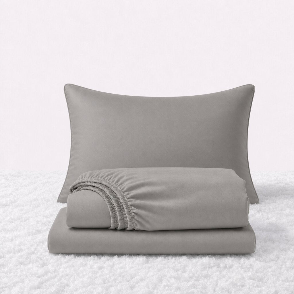 Light gray sheet set displayed with one pillow behind a folded fitted sheet and flat sheet on a white textured surface.