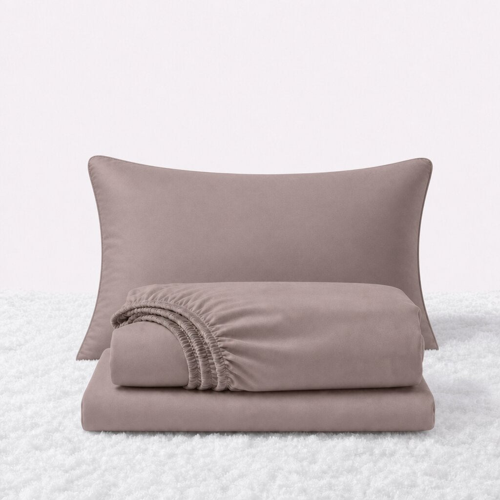 Blush pink sheet set displayed with one pillow behind a folded fitted sheet and flat sheet on a white textured surface.
