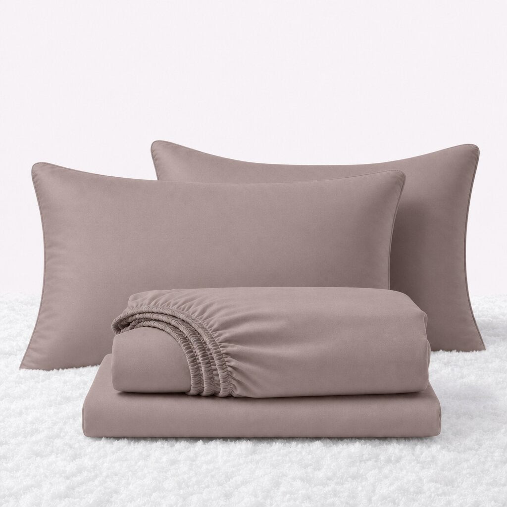 Blush pink sheet set displayed with two pillows behind a folded fitted sheet and flat sheet on a white textured surface.