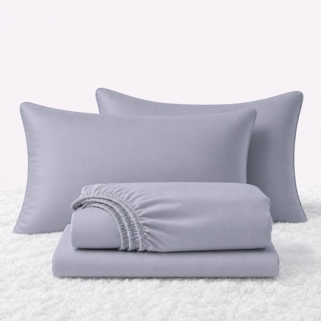 Pale blue gray sheet set displayed with two pillows behind a folded fitted sheet and flat sheet on a white textured surface.