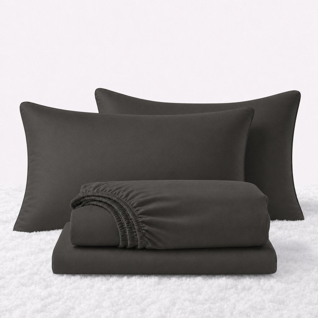 Dark gray sheet set displayed with two pillows behind a folded fitted sheet and flat sheet on a white textured surface.
