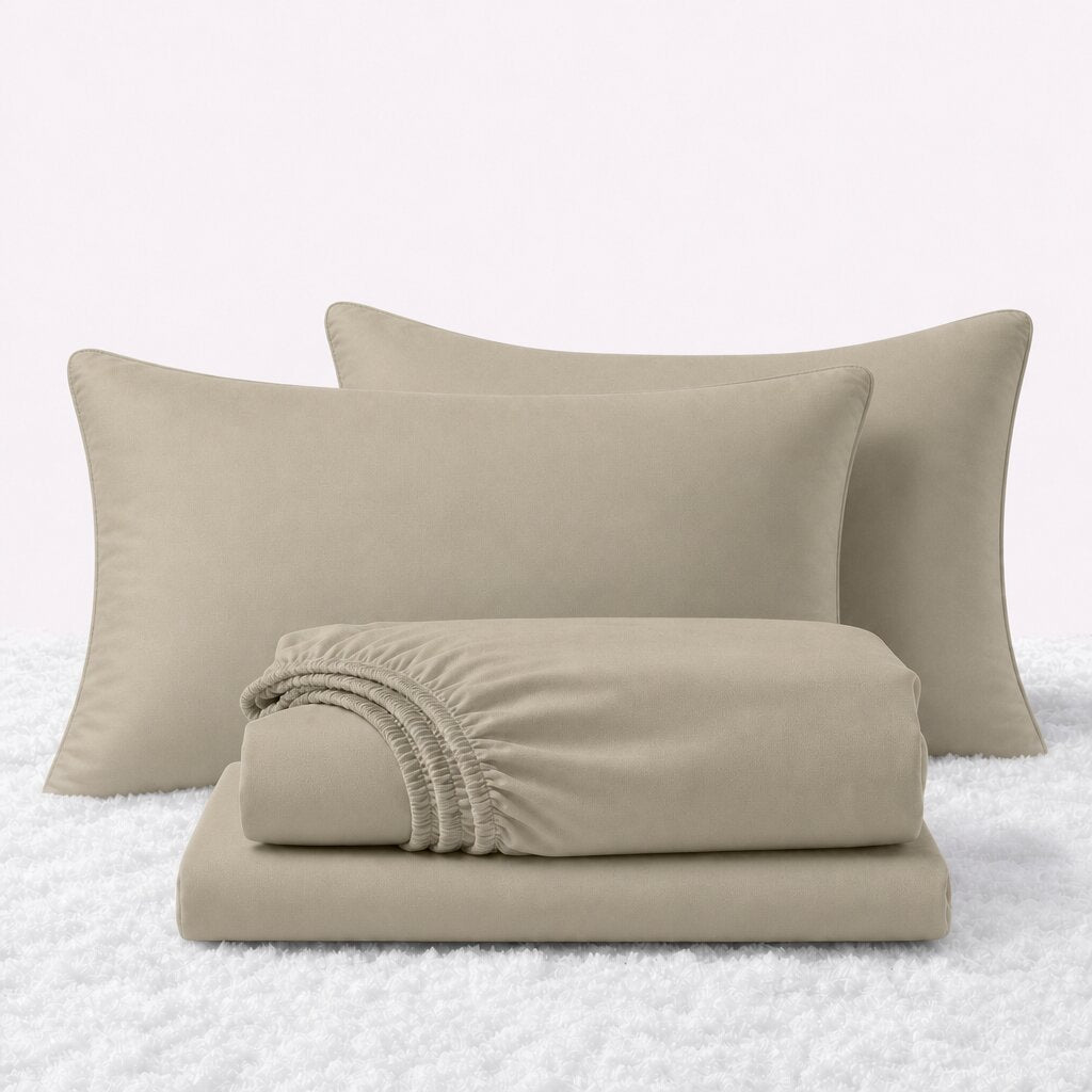 Cream sheet set displayed with two pillows behind a folded fitted sheet and flat sheet on a white textured surface.