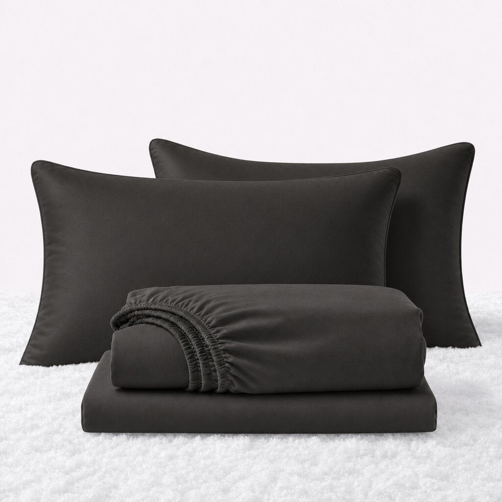 Charcoal gray sheet set displayed with two pillows behind a folded fitted sheet and flat sheet on a white textured surface.