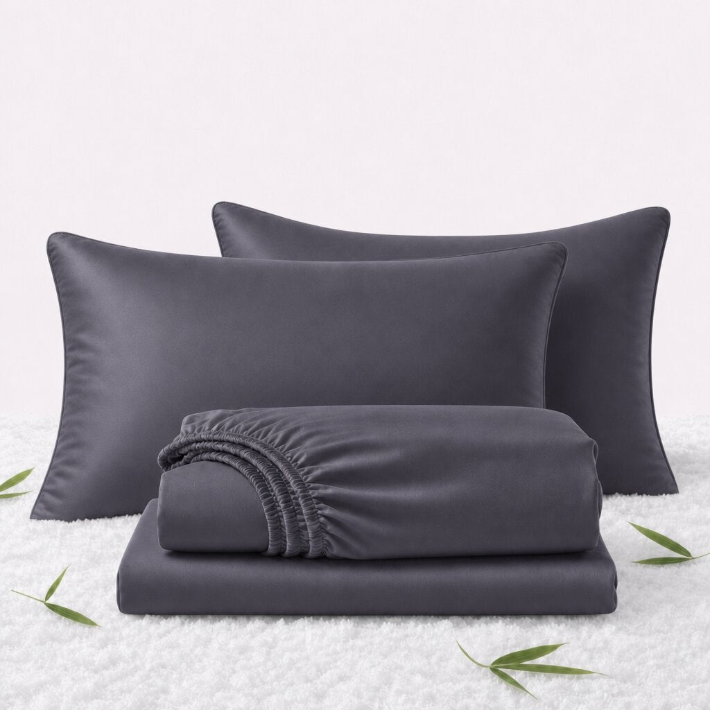 Folded dark gray sheets in front of 2 matching pillows on a white textured surface with scattered bamboo leaves.