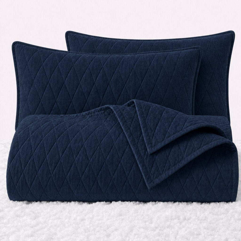 Folded navy blue diamond quilted cover with two matching pillow shams on a white textured surface.