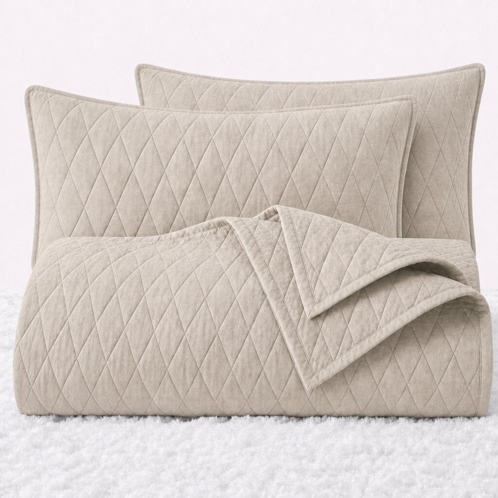 Folded ivory diamond quilted cover with two matching pillow shams on a white textured surface.
