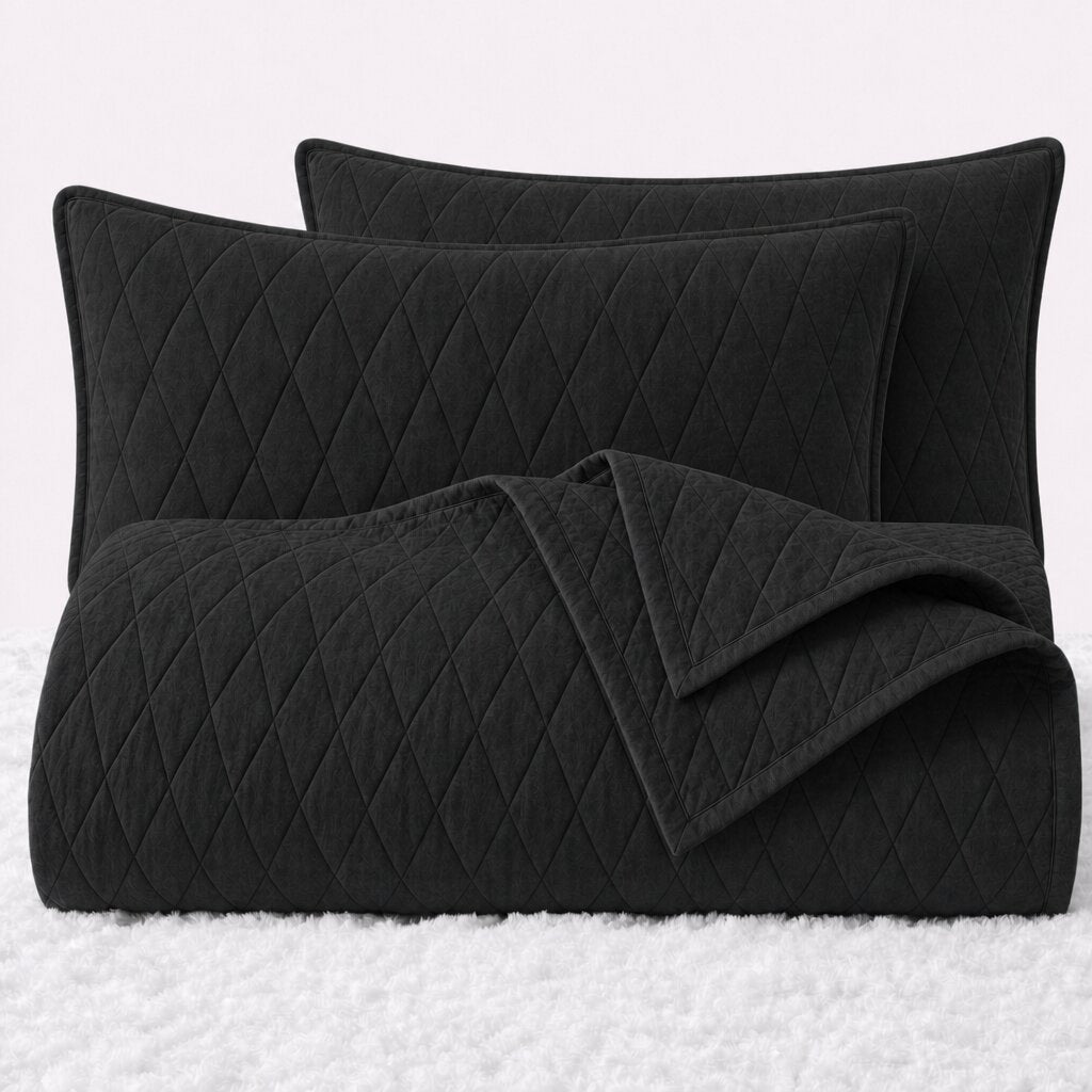 Folded black diamond quilted cover with two matching pillow shams on a white textured surface.