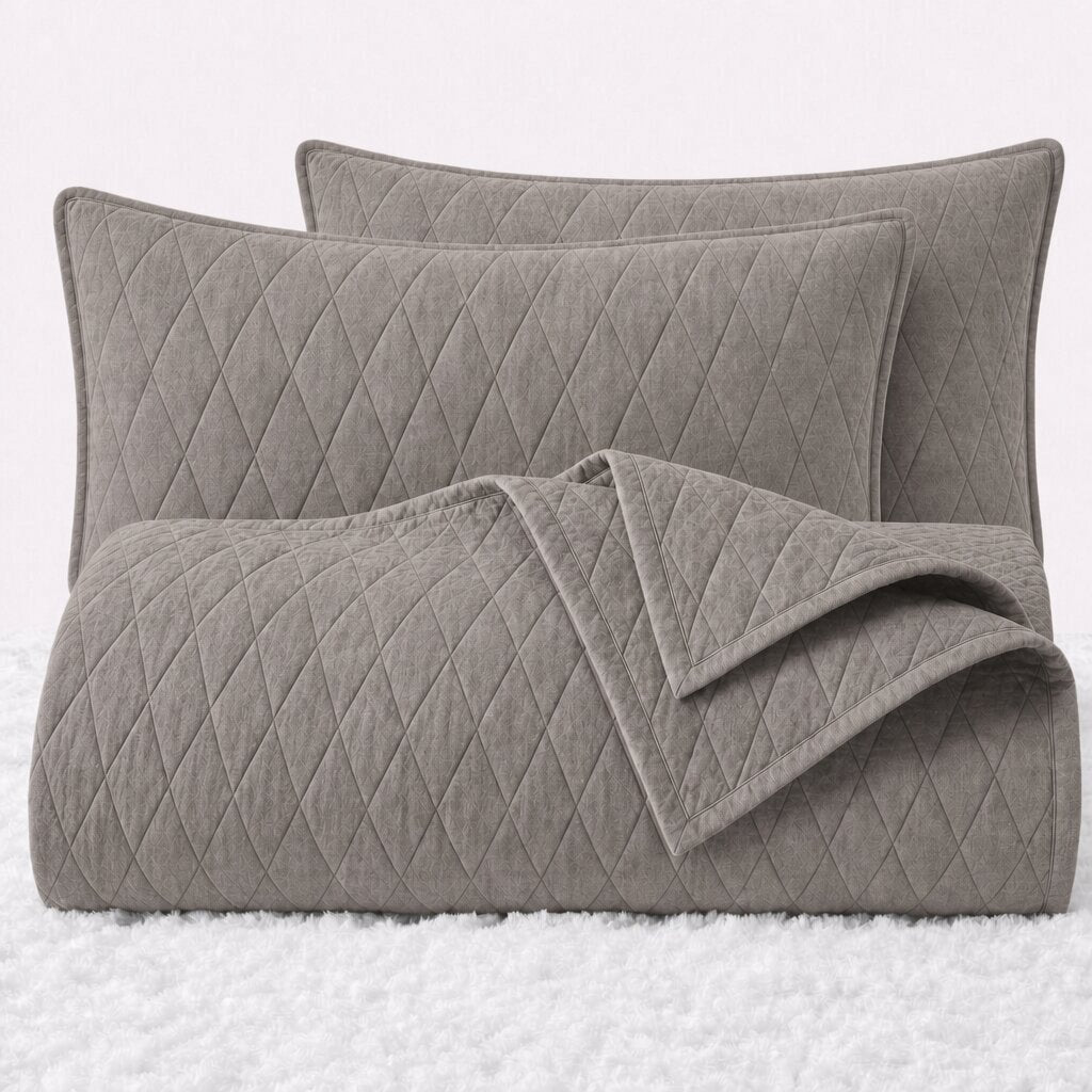 Folded taupe diamond quilted cover with two matching pillow shams on a white textured surface.