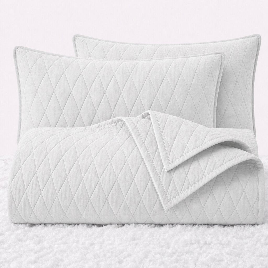Folded white diamond quilted cover with two matching pillow shams on a white textured surface.
