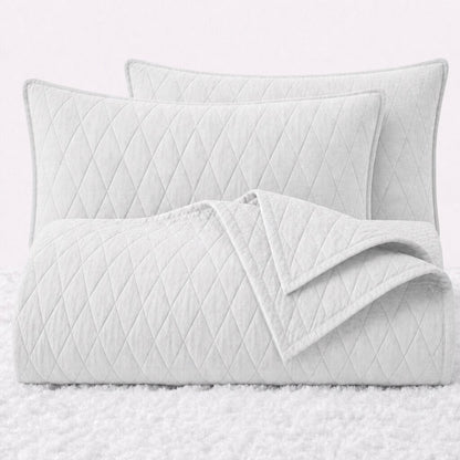 Folded white diamond quilted cover with two matching pillow shams on a white textured surface.